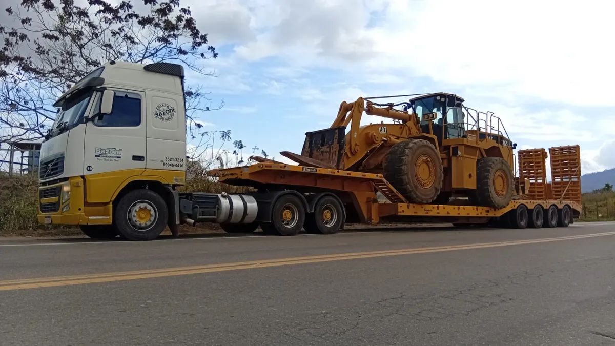 Carreta prancha transportando pá carregadeira CAT em rodovia