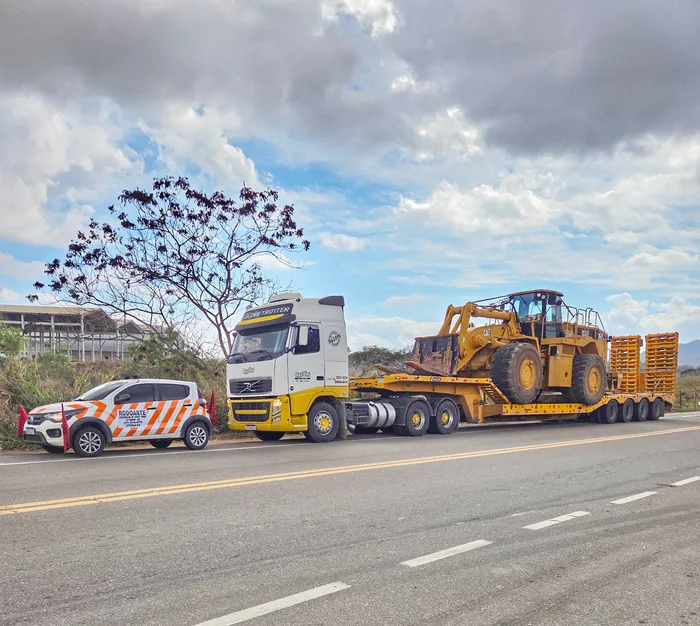 Pá carregadeira CAT em carreta prancha com veículo de escolta